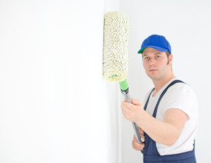 Painter In Uniform Paints The Wall. Focus On Roller Paint.