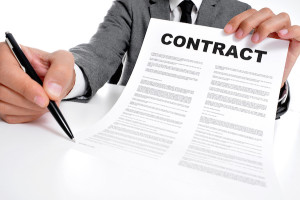 man wearing a suit sitting in a table showing a contract and where the signer must sign